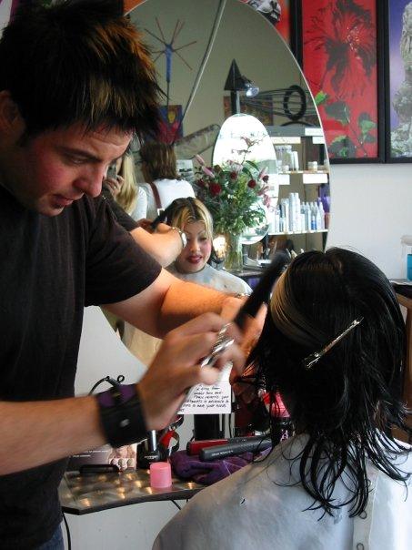 A young Christopher cutting a client's wet hair in front of a round salon mirror