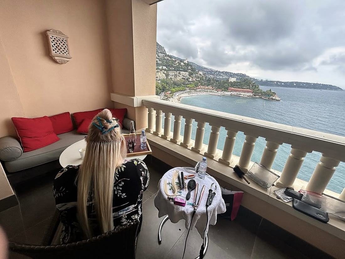 A client receiving keratin-tip extensions on a hotel balcony overlooking the Mediterranean
