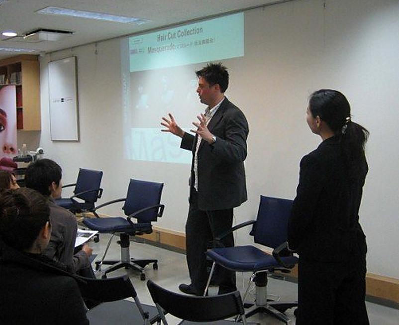 Christopher teaching a haircut collection to a seated class with a projected slide
