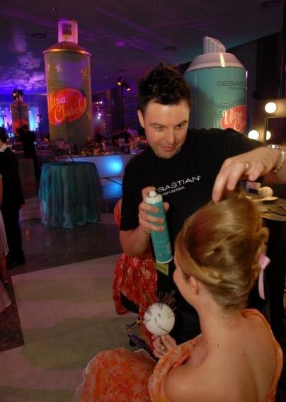 Christopher finishing a model's updo at a Sebastian event with giant hairspray cans