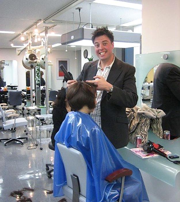 Christopher grinning while blow-drying a client in a salon in Japan