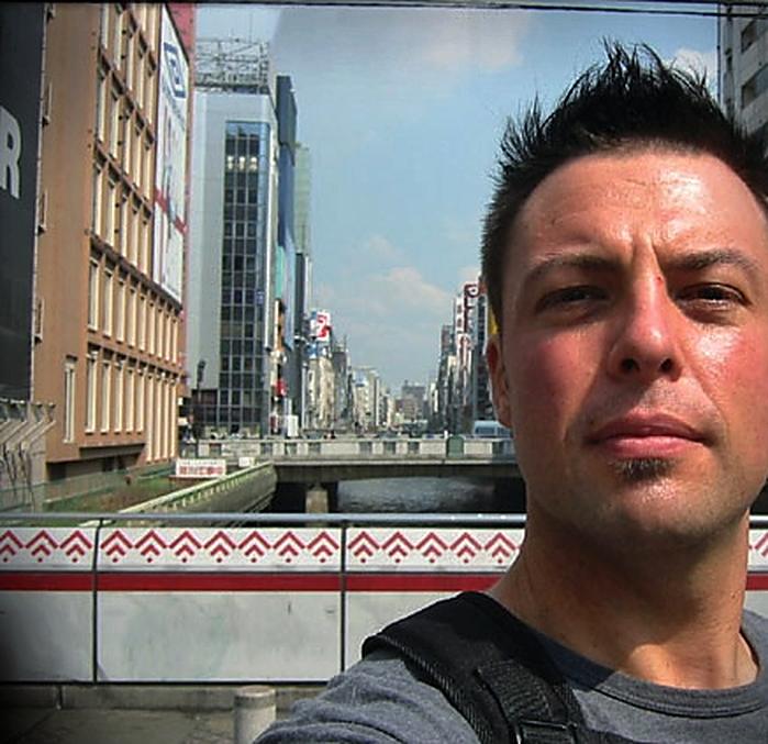 Christopher taking a selfie beside a canal lined with signs and buildings